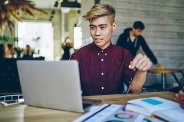 Düşünceli Asyalı hippi öğrenci modern laptop aygıtında kablosuz internet kullanarak internet üzerinden özel ders izliyor. Çinli genç adam dijital netbook üzerinde web sayfası tasarımı üzerinde çalışıyor.