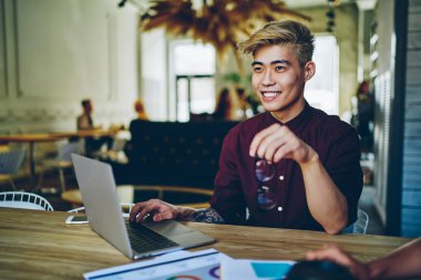 Gülümseyen Çinli öğrencinin yeni internet yayını hakkında düşünmesi ve modern dizüstü bilgisayardaki yazılımı güncellemesi. Netbook 'ta birlikte çalışma konusunda serbest çalışan başarılı Asyalı genç adam.