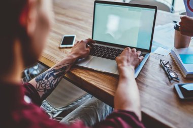 Modern bilgisayardaki sosyal ağlarda kablosuz internet bağlantısını kullanarak erkek elleri ve stil sahibi dövme sohbetlerinin kırpılmış görüntüsü. Uzaktan çalışma için dizüstü bilgisayardaki yazılımı güncelliyor