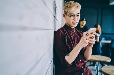 Gözlüklü Çinli hippi blogcu reklamınız için tanıtım alanının yanında duran akıllı telefondan gelen uyarıyı okuyor. Cep telefonuyla sohbet eden genç bir adam.