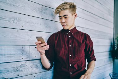 Düşünceli Asyalı hippi adam elinde akıllı telefonu tutuyor ve birlikte çalışırken duvarın yanında duran akıllı telefondan gelen mesajı okuyor. Çinli genç adam cep telefonuyla 4G internet kullanıyor.