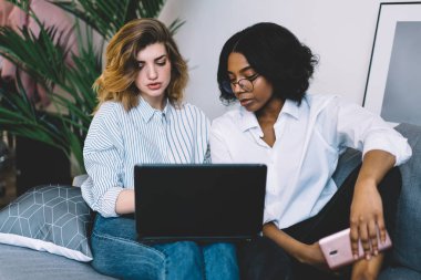 Kafkasyalı meslektaşı olan Afrikalı Amerikalı genç bir kadın modern apartmanda uzaktan çalışan kablosuz internet kullanarak kendi dizayn web sitesini geliştirmek için işbirliği yapıyor.