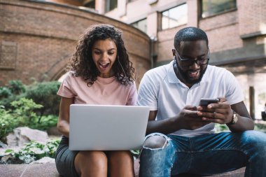 Şaşırmış hippi kız, favori web mağazasında indirimli indirimli alışveriş kuponuyla birlikte Afro-Amerikalı erkek arkadaşıyla şehir ortamında zaman geçirmesine şaşırmış.