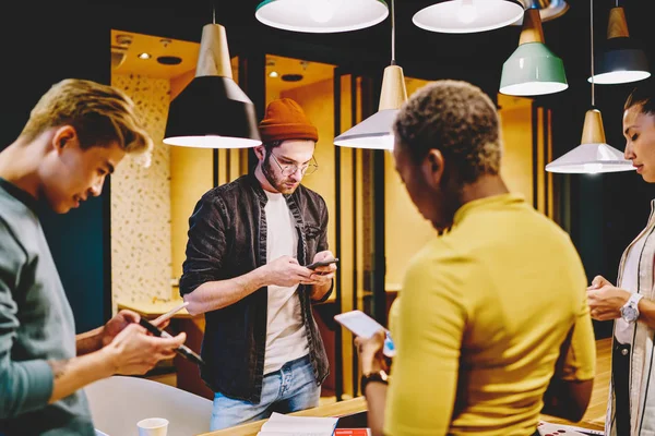 Group of hipsters ignore real communication using mobile phones for networking, crew of young multiracial millennial students checking social networks update via smartphones in coworking offic