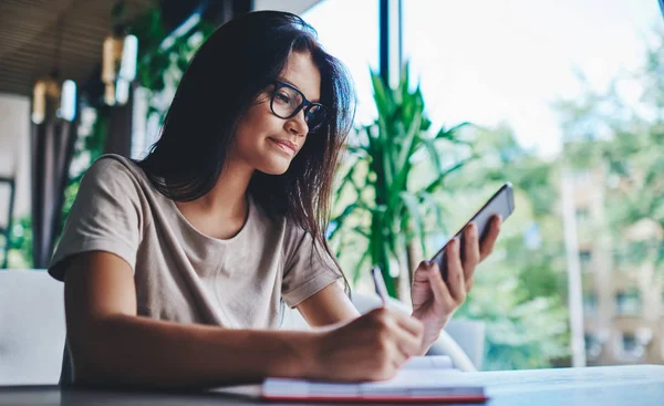千年期高加索女性在咖啡店用手机阅读社交网络新闻 女性博主则在智能手机上做在线研究 — 图库照片