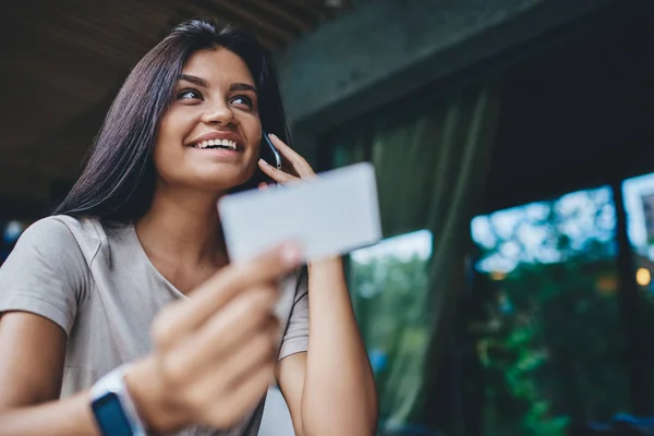 Happy young caucasian woman happy about holding discount card for booking calling to service operator, cheerful hipster girl checking banking balance on credit card having mobile phone conversation