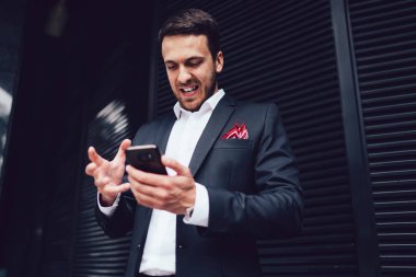 Kızgın adam, döviz parasıyla ilgili şirket anlaşmasını bozmakla ilgili sorunlu bilgilerle e-posta aldı. Stresli erkek bankacı, ödeme işlemlerini mobil uygulama çözme hatalarıyla kontrol ediyor.