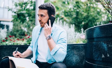 Kafkasyalı hippi operatörle hizmet danışmanlığı için cep telefonu cihazıyla arıyor. Çizim defteri olan ciddi bir erkek, şehir merkezinde internet üzerinden cep telefonundan aranmış.