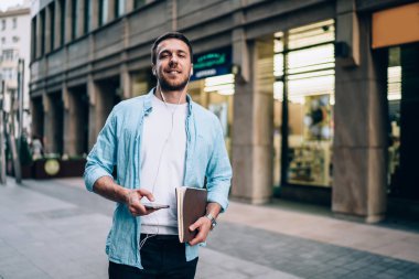 En sevdiği müzik listesinin, elektronik kulaklıklı mutlu adamın, elinde cep telefonu cihazıyla kameraya gülümseyen yakışıklı, pozitif hipster bir adamın yarım boy portresi.