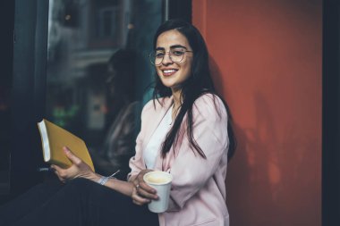 Neşeli İspanyol erasmus öğrencilerinin portresi kahveyle dinleniyor eğitim kitapçığıyla planlama sürecinin peşinden gitmek için dışarıda kameraya gülümseyen bilgi notları olan pozitif kadın.