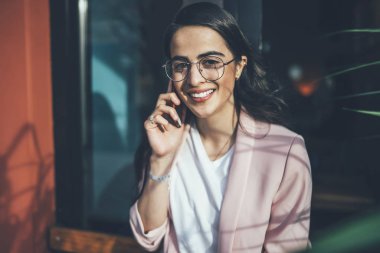 Gözlüklü gülümseyen hippi kızın portresi cep telefonuyla konuşan cep telefonu görüşmeleri için gümrük vergileriyle tatmin olmuş, pozitif Gürcü kadın kameraya bakıyor ve akıllı telefondan sohbet ediyor.