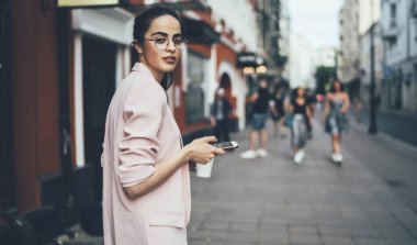 Çekici İspanyol kadın blog yazarının yarı boy portresi cep telefonu aygıtıyla uluslararası şehri keşfetmek için kameraya bakıyor, modern teknoloji kavramı ve çevrimiçi telefon.