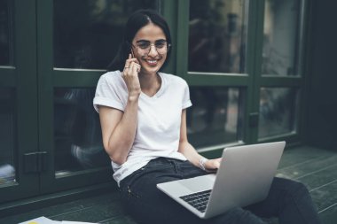 Modern netbook cihazıyla öğrenme sırasında kameraya gülümseyen klasik optik gözlüklü neşeli hipster öğrenci portresi, telefon etmek için gezinen interneti kullanan mutlu Gürcü grafik tasarımcısı