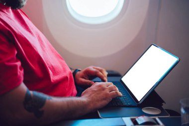 Uçaktaki kablosuz internete dokunmatik ped ile bağlanan genç bir uçuş yolcusu uçak kabin penceresinin yanında oturuyor. Ağ şablonu için boş ekranı, serbest çalışma için dijital göçebe işini düzenle