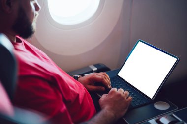 Uçaktaki kablosuz internete dokunmatik ped ile bağlanan genç bir uçuş yolcusu uçak kabin penceresinin yanında oturuyor. Ağ şablonu için boş ekranı, serbest çalışma için dijital göçebe işini düzenle
