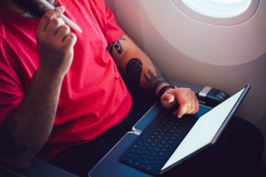 Uçaktaki kablosuz internete dokunmatik ped ile bağlanan genç bir uçuş yolcusu uçak kabin penceresinin yanında oturuyor. Web şablonu için boş ekranı yapılandırın, iş planlaması hakkında düşünün