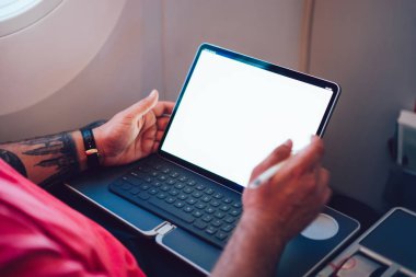 Uçaktaki kablosuz internete dokunmatik ped ile bağlanan genç bir uçuş yolcusu uçak kabin penceresinin yanında oturuyor. Ağ şablonu için boş ekranı düzenle, kalem ile tablete dokun