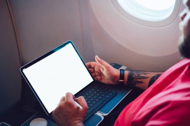 Uçaktaki kablosuz internete dokunmatik ped ile bağlanan genç bir uçuş yolcusu uçak kabin penceresinin yanında oturuyor. Ağ şablonu için boş ekranı düzenle, kalem ile tablete dokun