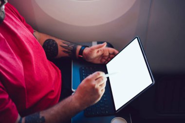 Uçaktaki kablosuz internete dokunmatik ped ile bağlanan genç bir uçuş yolcusu uçak kabin penceresinin yanında oturuyor. Ağ şablonu için boş ekranı düzenle, kalem ile tablete dokun