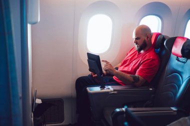 Uçak kabin camının yanında rahat bir uçak koltuğunda otururken uçakta film izleyen genç adam. Beyaz adam birinci sınıf seyahatin tadını çıkarıyor.