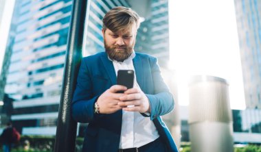 Ciddi profesyonel değişim uzmanı cep telefonu ve metin stratejisi ile şehir merkezinde duruyor, cep telefonu cihazıyla beyaz adam dışarıda iş ortağı bekliyor SMS 'leri kontrol ediyor.