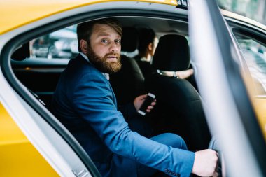 Resmi olarak beyaz erkek bankacının portresi taksideki iş gezisinde kameraya bakarken taksinin kapısının önünde cep telefonu cihazıyla 30 'lu yaşların gururlu CEO' sunun portresi.
