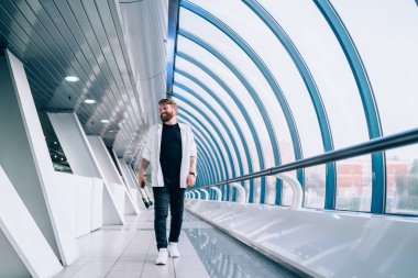 Pozitif sakallı bir adam, modaya uygun giyinmiş, halka açık bir yerde yürüyor ve gülümsüyor, neşeli bir beyaz erkek, varış yerine gidiyor, güzel görünümlü hippi çocuk.