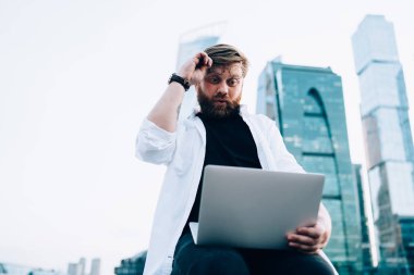 Heyecanlı erkek blogcu dışarıda içerik metni okurken dizüstü bilgisayar istatistiklerinden gelen şaşkınlığa uğramış, internetteki web sitesini izleyen hipster hayranı adam Netbook 'taki içerikten hayrete düşmüş.