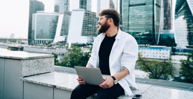 Şehir merkezinde açık modern dizüstü bilgisayarla statup projesini hayal eden olumlu erkek yazılım geliştirici. Şehir merkezinde internet ortamında çalışan serbest çalışan bir erkek.