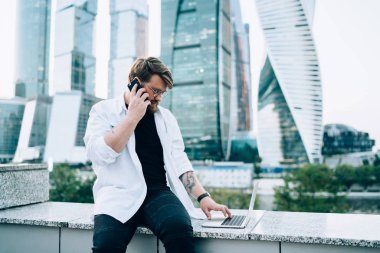 Genç bir erkek yeni uygulama ile akıllı telefon görüşmesi yapıyor, yetenekli bir iş adamı internette dolaşma konusunda operatöre açık dizüstü bilgisayarla arıyor.