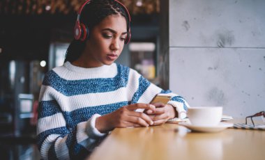 Akıllı telefon cihazları ve bluetooth kulaklıklarla ilginç ses kitapları dinleyen çekici bir kadın. Elektronik kulaklıkla müzik kaydından hoşlanan genç hippi kız SMS okuyor.