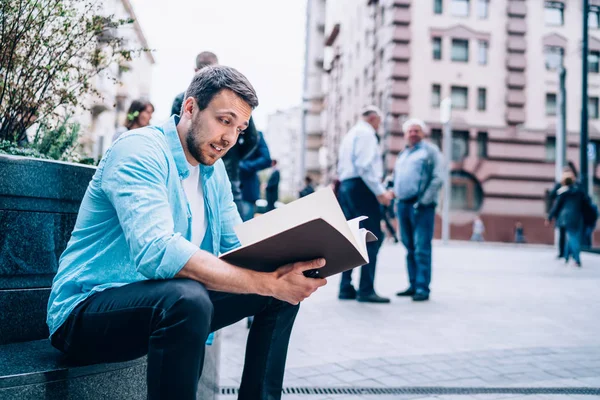 驚くべき男性学生は 都市の環境に座ってカジュアルなスタイリッシュなアパレルを身に着けていると教育のための教科書から情報を学ぶ 路上で知的ヒップスター男性読書メモ — ストック写真