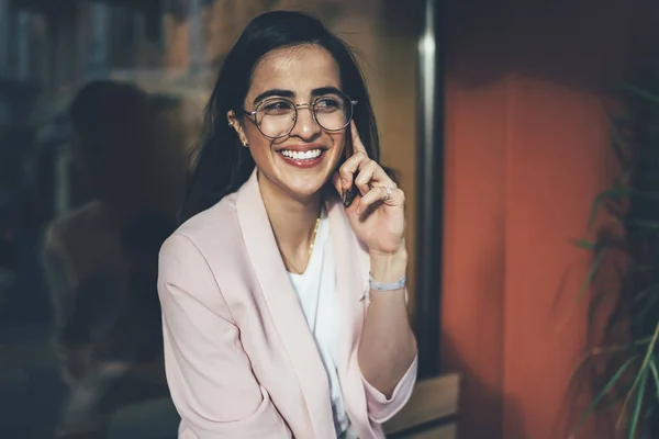 Cheerful Georgian female in casual wear happy to hear friend calling using international operator tariff in roaming spending free time sitting on urban setting, concept of online communication