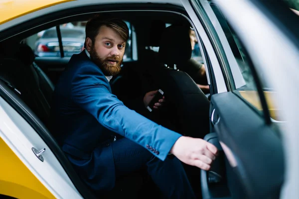 Portrait of handsome bearded man in formal suit looking at camera while getting to business meeting in financial district of Manhattan, Caucasian corporate director sitting on passenger seat in taxi