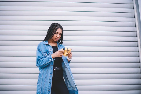 Concentrated female photographer holding vintage camera in hands and editing photos on publicity area, serious african amateur recalls pleasant moments from pictures on old fashioned equipment