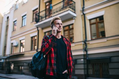 Sırt çantalı bir adam sokakta akıllı telefondan konuşuyor.