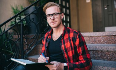 Ciddi bir adam sokakta not defteri yazıyor.