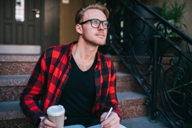 Sıcak içkili bir adam yazı yazıyor ve uzaklara bakıyor.