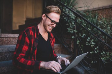 Basamaklarda dizüstü bilgisayar kullanan neşeli serbest yazar.