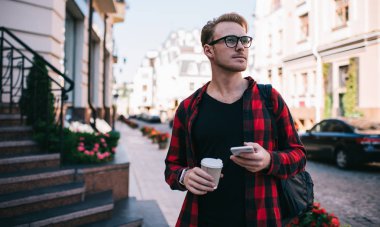 Sıcak içkisi ve akıllı telefonu olan düşünceli bir adam başka tarafa bakıyor.