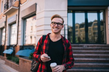 Akıllı telefonlu neşeli adam ve sokakta sıcak bir içecek.