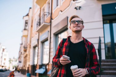 Akıllı telefonu ve sıcak içeceği olan gülümseyen adam yukarı bakıyor.