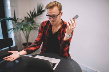 Akıllı telefonlu asabi serbest yazar dizüstü bilgisayara bakıyor.