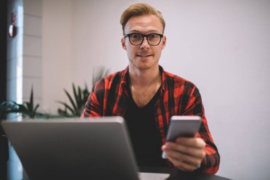 Akıllı telefonlu yakışıklı serbest çalışan kameraya bakıyor.