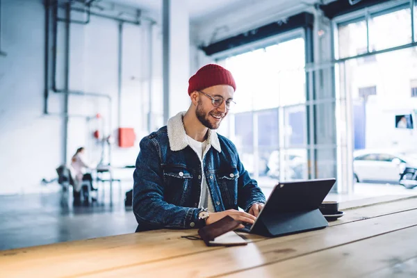 Positive male blogger browsing profile in networks on touch pad via 4G internet connection working in modern coworking space, young man chatting online on digital tablet enjoying virtual communication