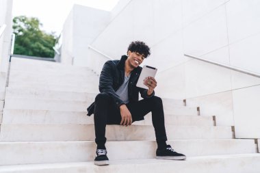 Mutlu Latin hipster adam şehir merdivenlerinde dinleniyor. Haberleri okuyor ve dijital tabletle komik bilgilere bakıyor. Kablosuz internet bağlantısı var.
