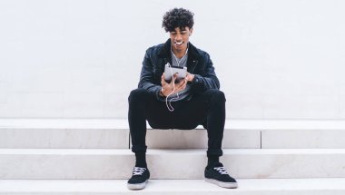 Neşeli milenyum hipster 'ı tanıtım geçmişi olan şehir merdivenlerinde dinleniyor ve favori müzik podcast' inin ses kitaplarıyla uygulama yüklemek için boş zaman harcamasını dinliyor.