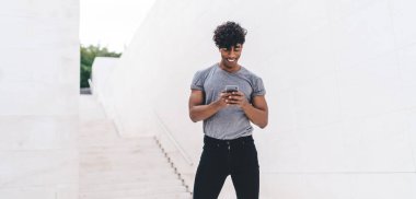 Gülümseyen genç adam akıllı telefondan mesaj yolluyor. Şehir merkezindeki internet ortamında duruyor. Sosyal ağda internet bağlantısı olan cep telefonu kullanan olumlu trend hipster blogu yazıyor.