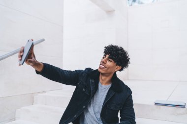 Hücresel cihazda fotoğraf çekerken gülümseyen hippi adam grup sohbetinde sanal arkadaşlara poz veriyor. Neşeli adam ön kamerayla boş zamanlarında fotoğraf çekiyor.