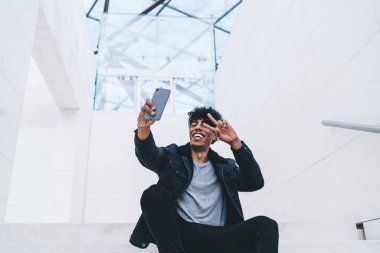 Neşeli hippi, modern akıllı telefonun ön kamerasında özçekim yapıyor. Bloglar için dışarıda zaman geçiriyor. Dijital cep telefonu aygıtı aracılığıyla Ziyaretçi işaretleri gösteren mutlu bir erkek.